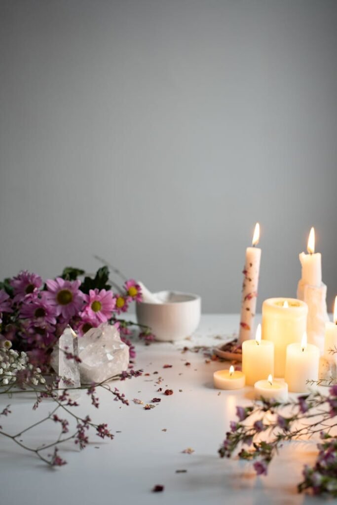 A calming arrangement of candles, flowers, and crystals on a white table.