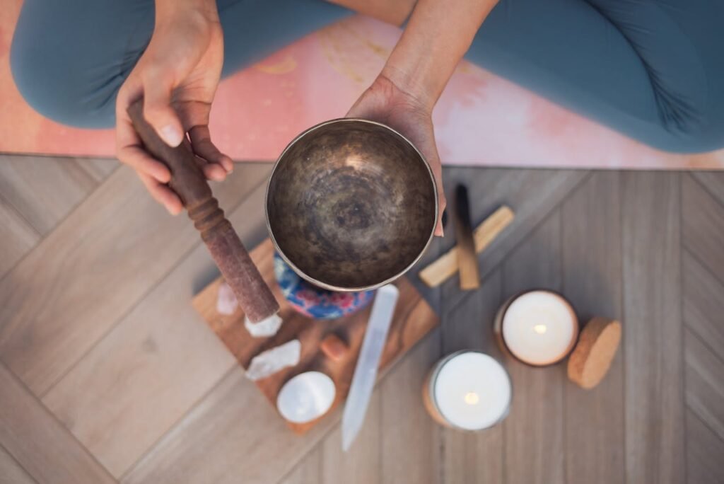 A person holding a Tibetan singing bowl on a yoga mat with meditation tools.